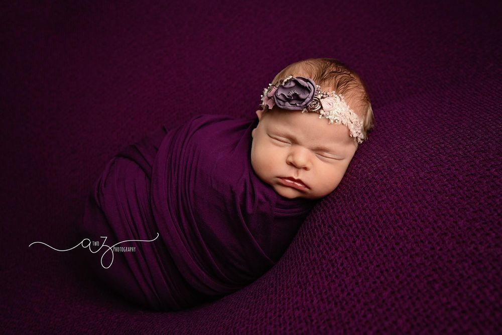 Artistic newborn portrait with baby wrapped in deep purple fabric wearing delicate headpiece.