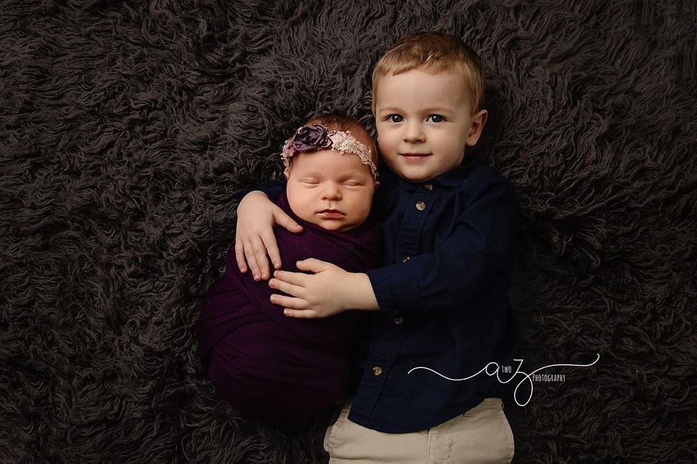 Sibling portrait featuring toddler and newborn on dark furry backdrop.