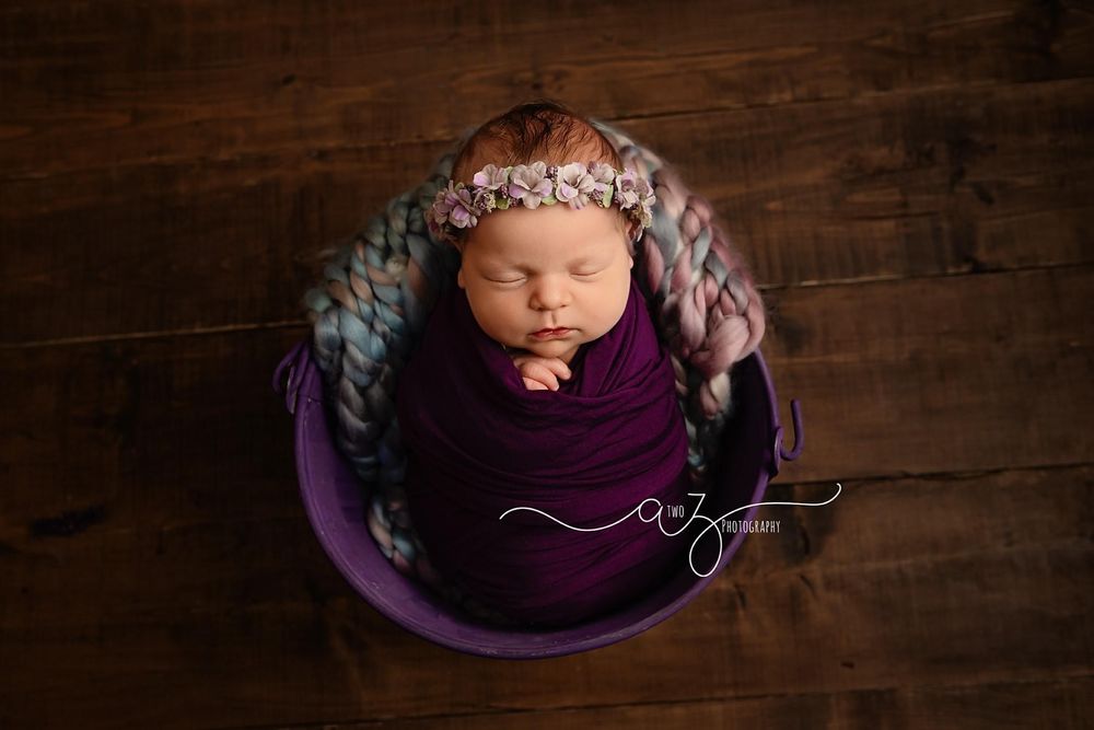 Overhead view of sleeping baby in purple wrap positioned in wooden bowl.