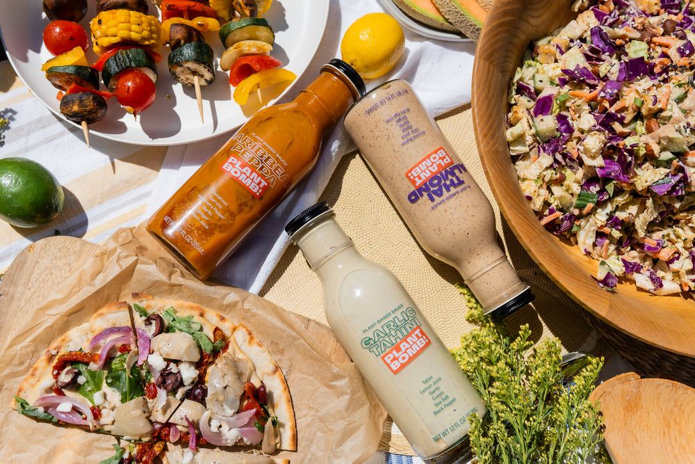 Food product photography of an overhead shot of grilled kabobs, bottled drinks, tacos and a large salad bowl in bright natural lighting.
