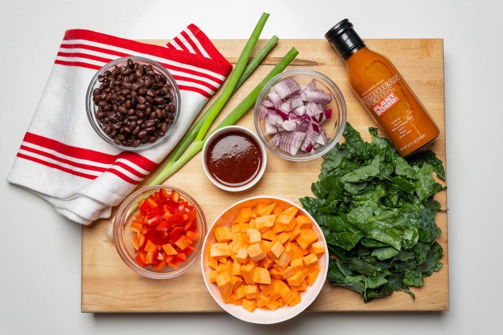 Food photography Ingredients for cooking displayed on wooden board including red beans, celery, onions, tomatoes, carrots, and leafy greens.