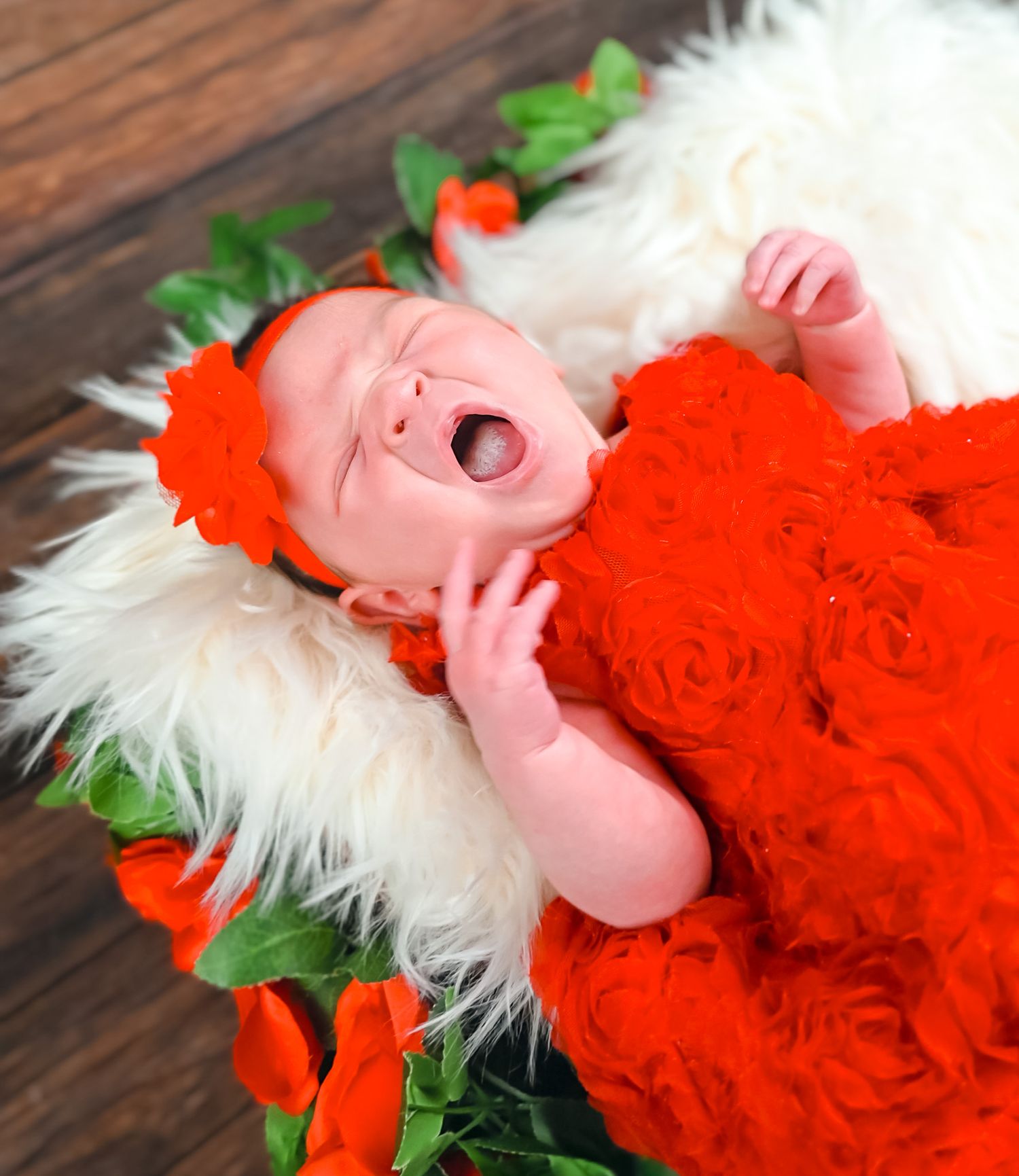 Sleeping newborn in red dress on white fur with floral accents.