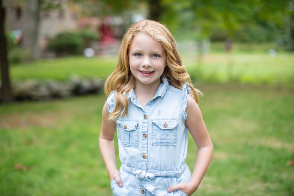 Young person in denim vest posing against blurred natural outdoor background.