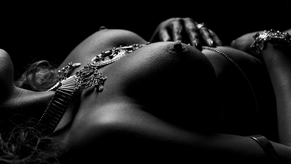Artistic black and white nude torso with jewelry in dramatic lighting against dark background.