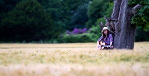 lady sitting under a tree playing a guitar