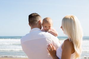 Family in white outfits embracing together while enjoying sunny day at beach.