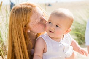 A tender moment between parent and baby surrounded by beach grass on a sunny day.