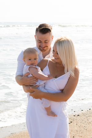 A family wearing white outfits shares a tender moment together on a sunny beach.