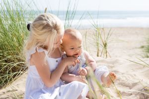 A sweet interaction between parent and baby on a beach with dune grass swaying in the background.