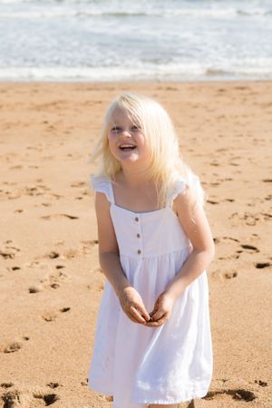 Person in a white summer dress laughs joyfully on a sunny beach.
