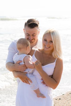 A young family shares joyful moments together on a sunny beach wearing matching white outfits.