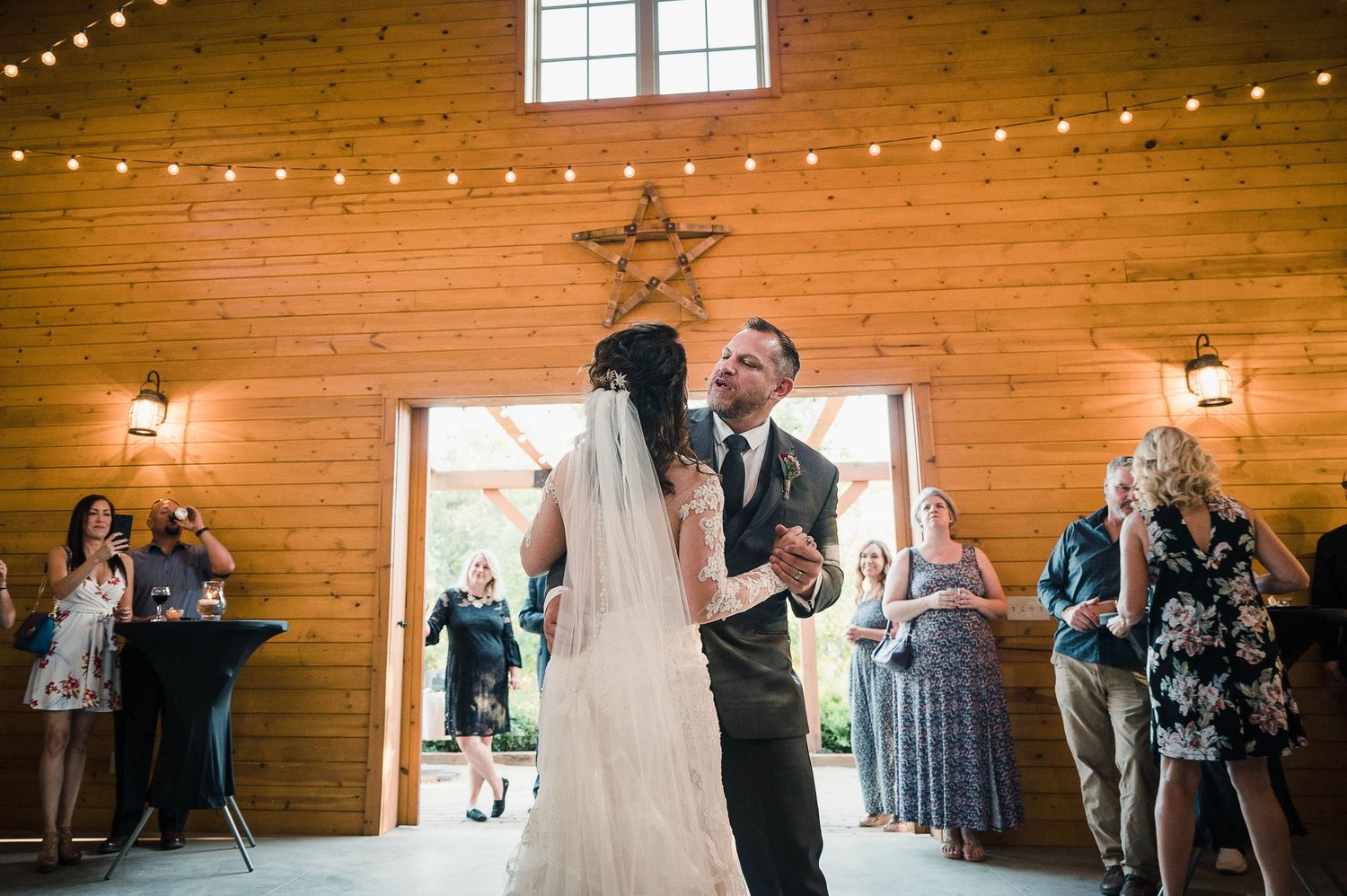 Wedding celebration in a wooden barn with string lights and rustic star decor overhead.