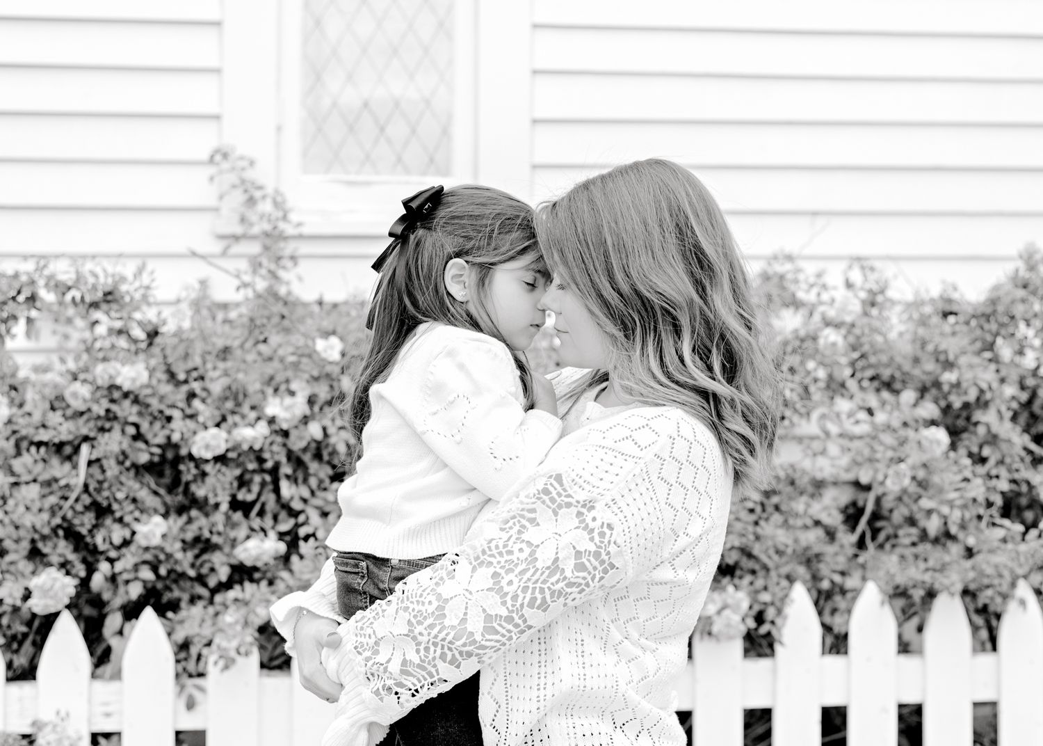 A touching black and white portrait shared between mother and daughter against a white picket fence background.