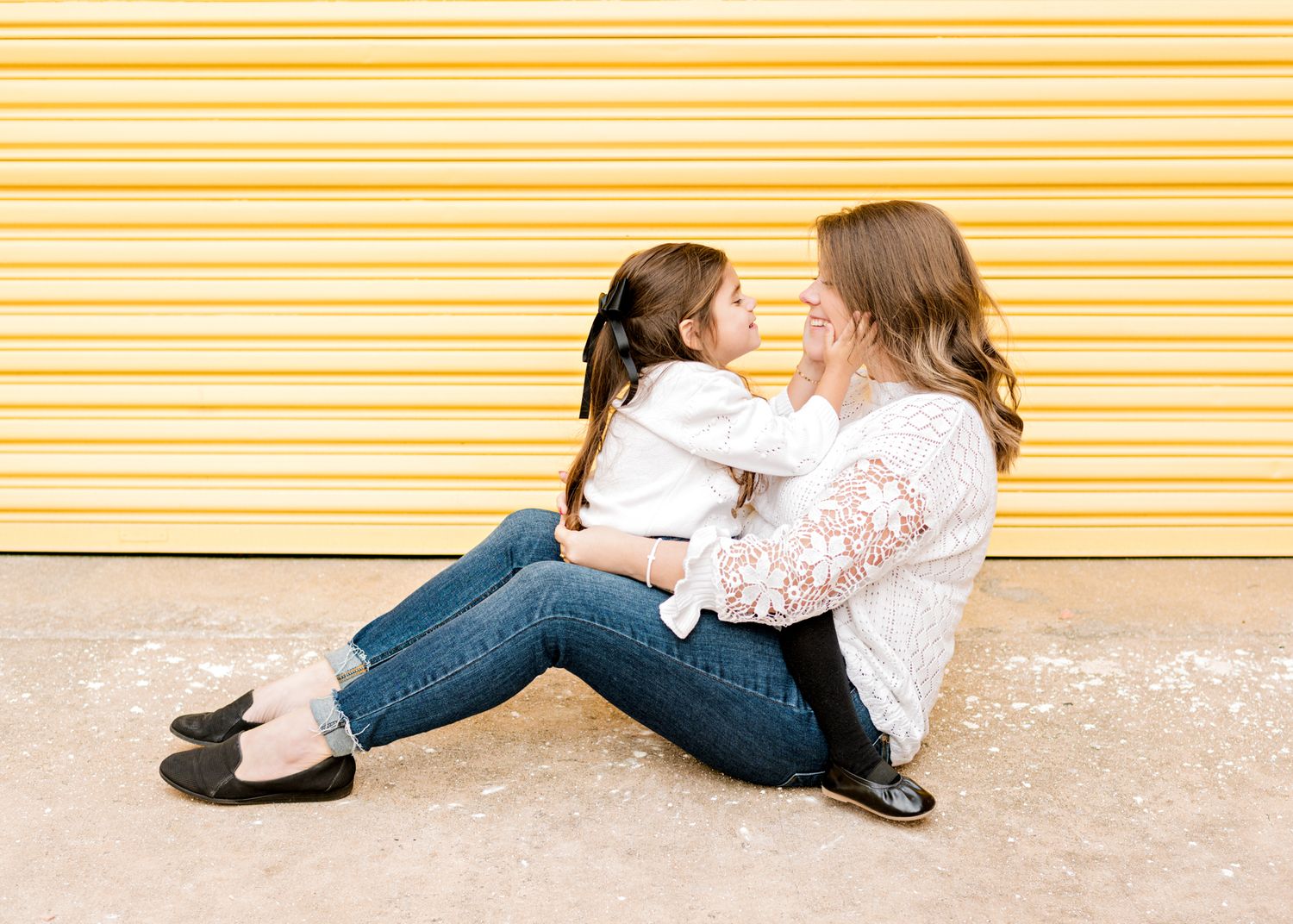 Two people in white tops and jeans share an intimate moment against a yellow striped wall.
