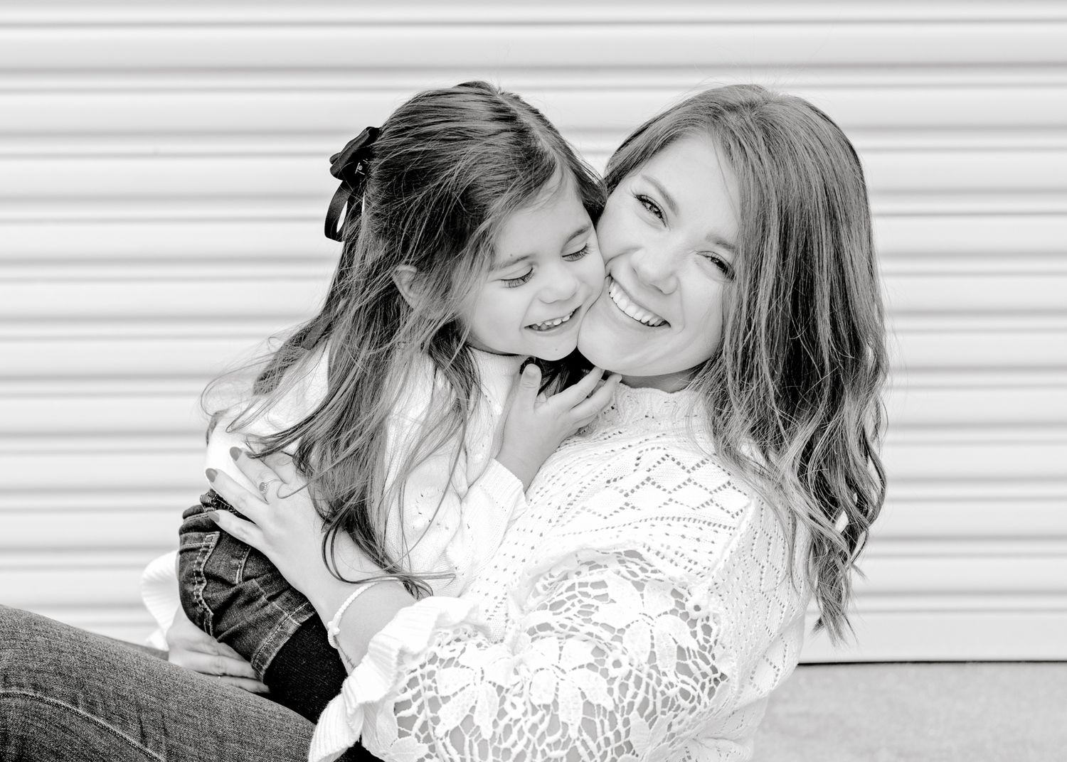 Black and white portrait capturing joyful embrace against textured wall background.