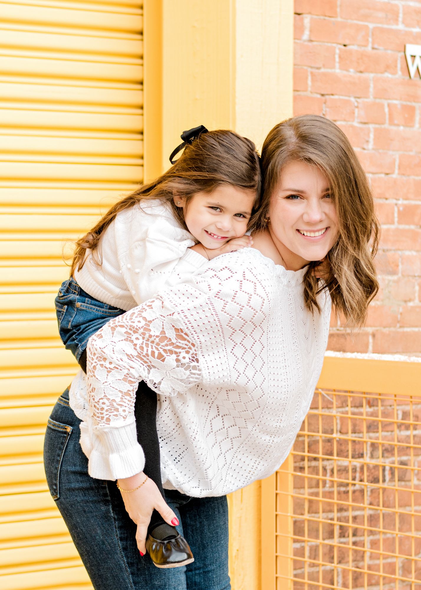 Heartwarming piggyback ride moment against yellow and brick wall backdrop.