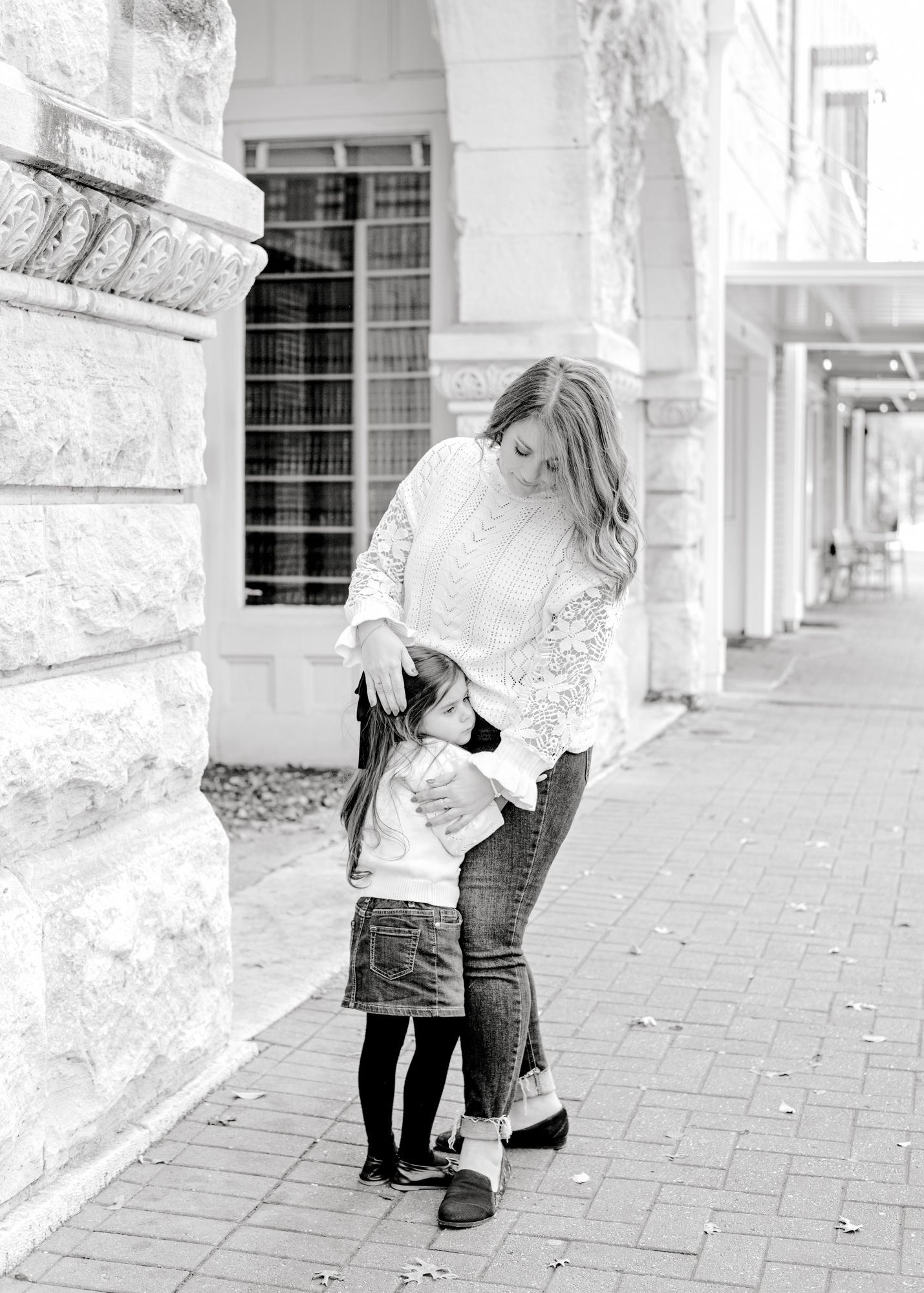 Parent and child share a tender moment together along a historic columned walkway in black and white.