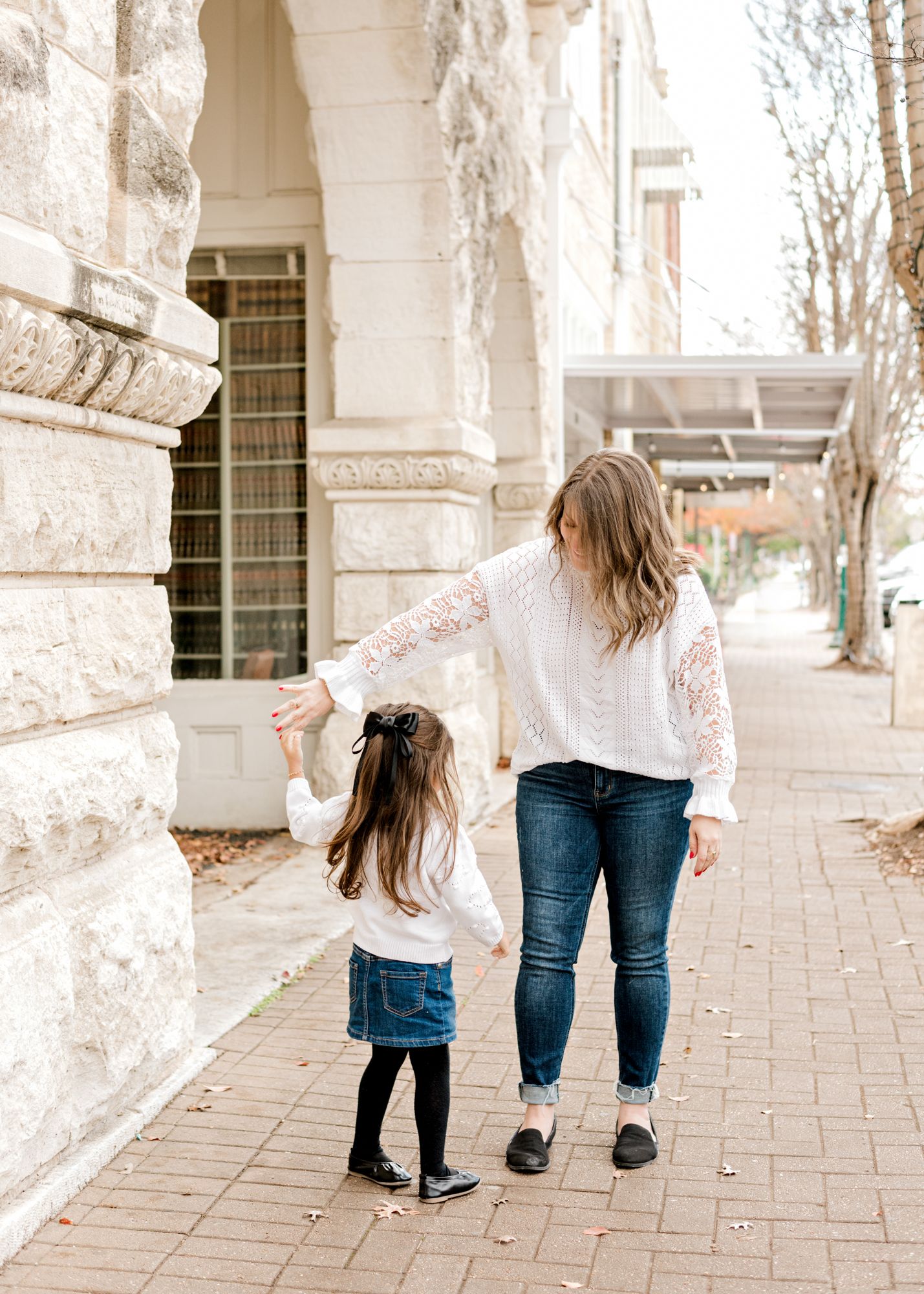A pair walk together along a columned walkway in matching white lace tops and jeans.
