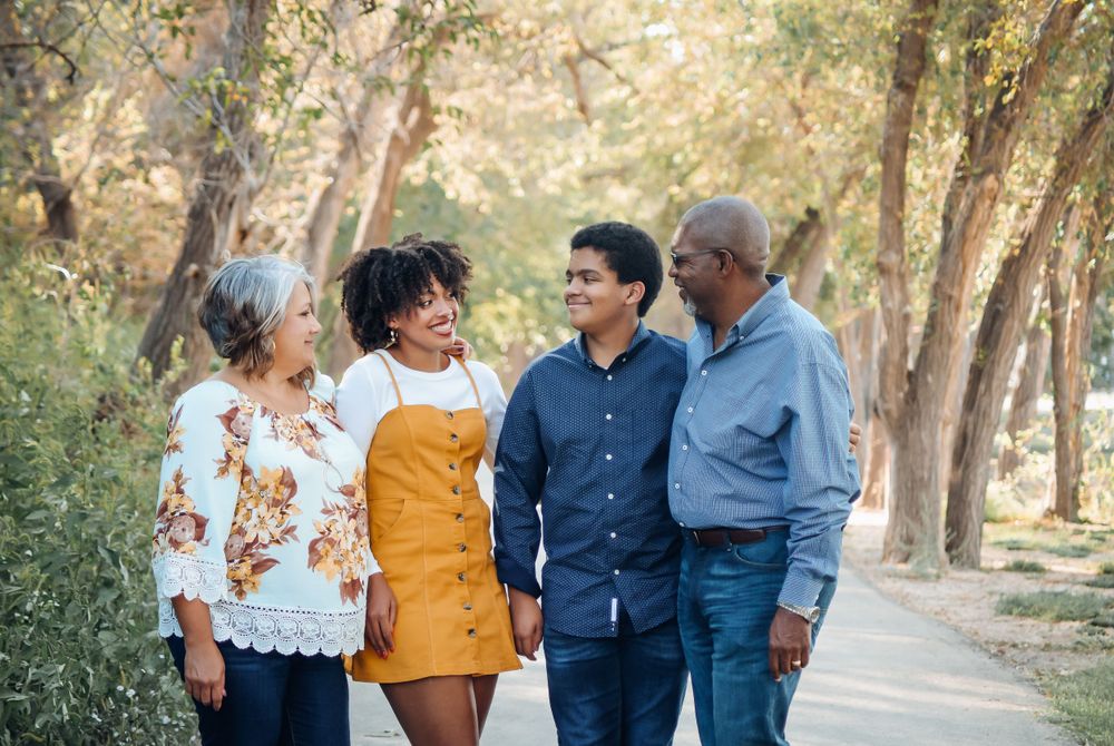Family walking together through a tree-lined path during an outdoor photo session.
