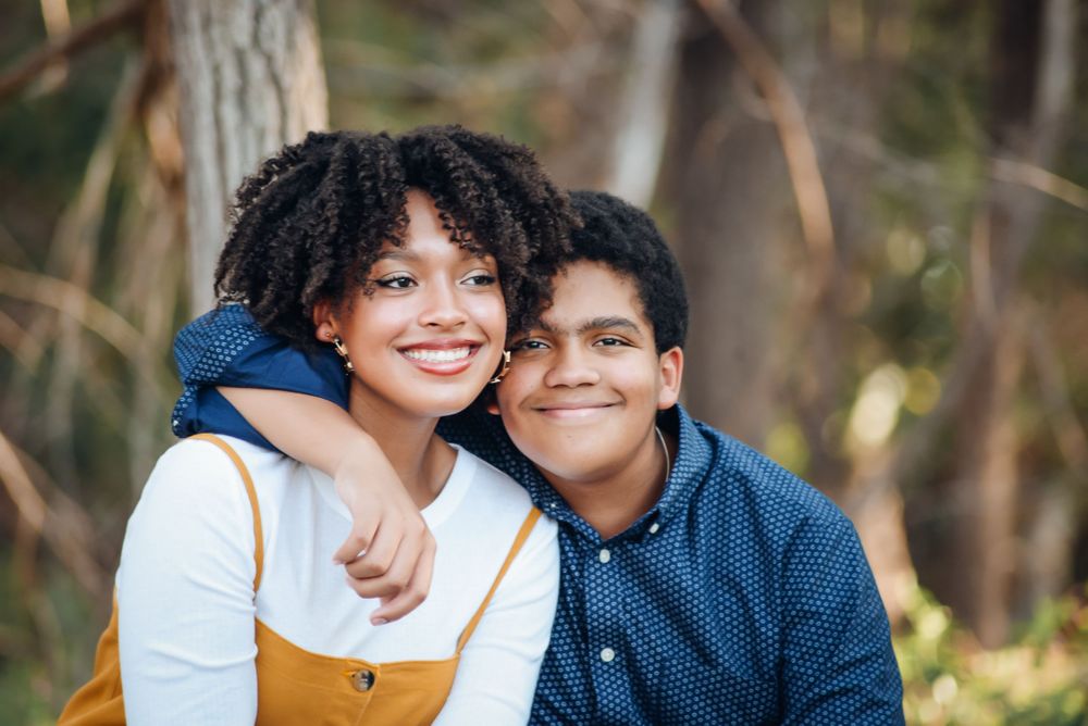 A couple shares a tender moment while sitting together on grass in a park setting.
