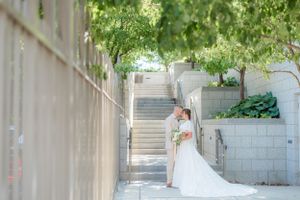 Bride and groom embrace near stone steps surrounded by green trees at their outdoor wedding venue. Megan Snell Photo Utah Weddings temple