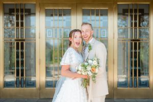 Joyful bride and groom laugh together in front of golden draper temple doors holding a bridal bouquet. Megan Snell Photo Utah Weddings