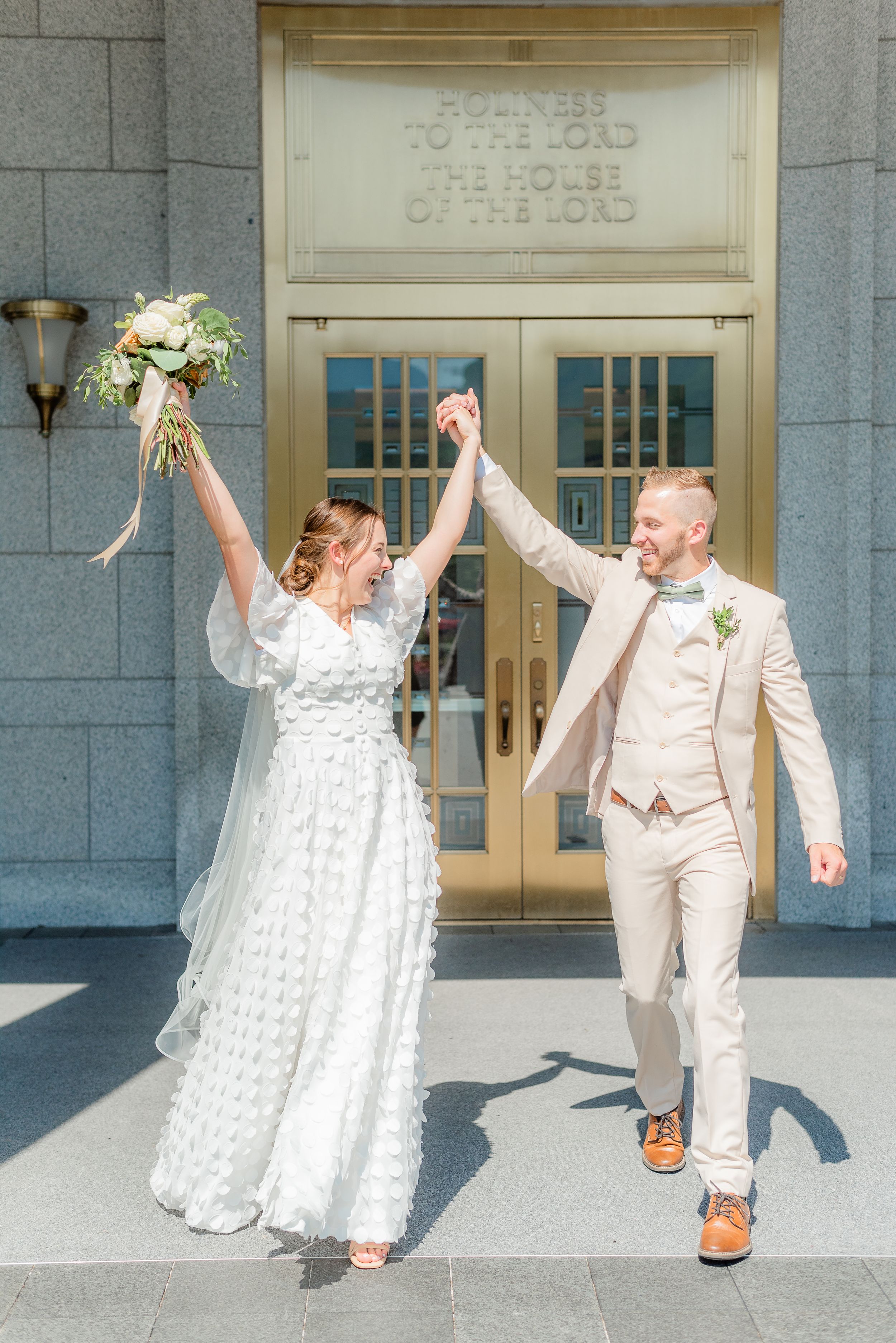 Joyful bride and groom raise hands in celebration outside LDS temple doors on their wedding day.