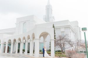 Bride and groom stand together outside a white LDS temple with arched columns on their wedding day.