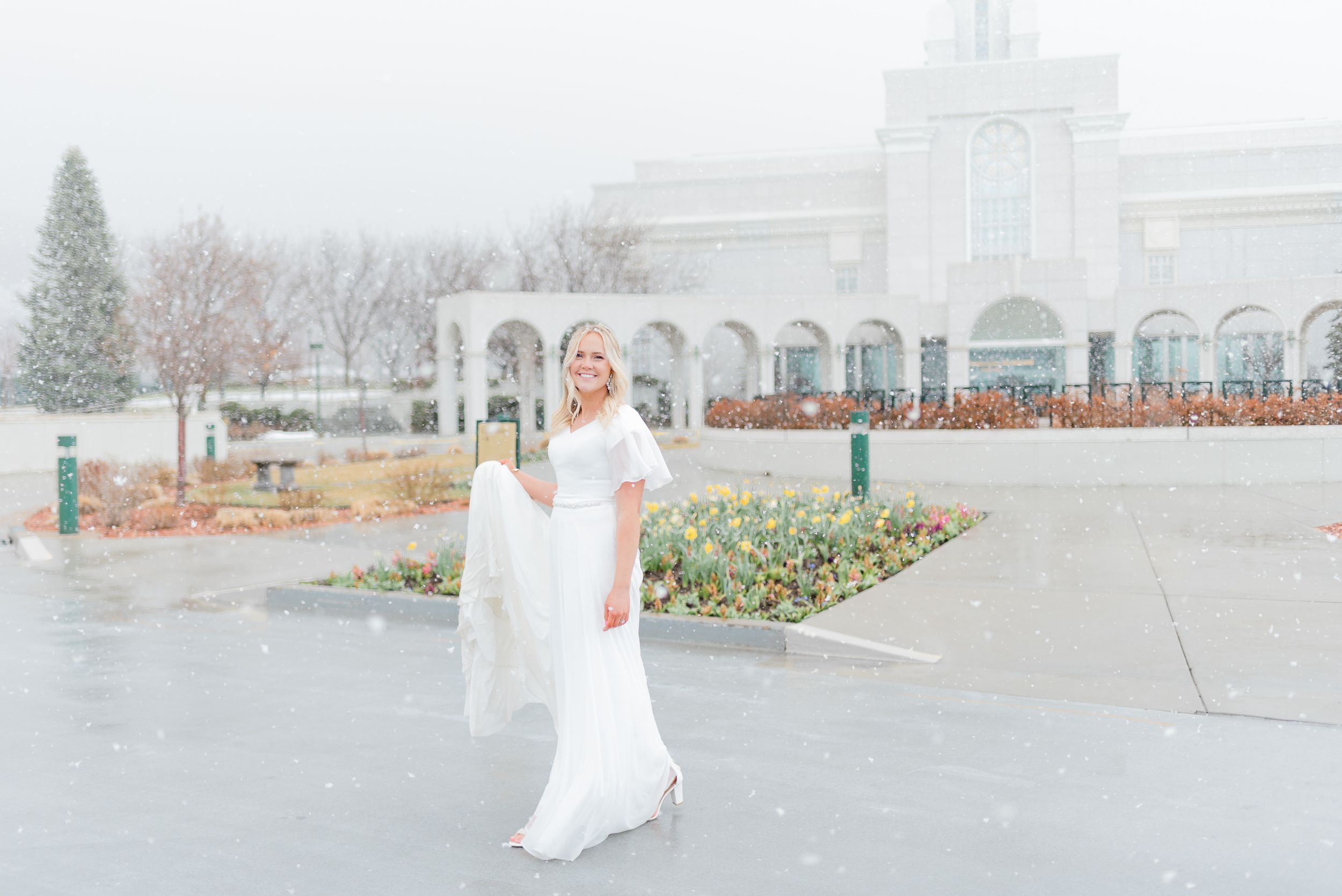 Bride in white wedding dress twirls gracefully outside an LDS temple during a snowy winter wedding.