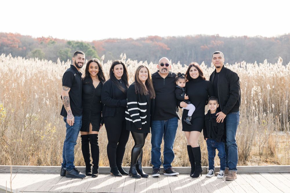 A large family group poses together in casual attire against an autumn field backdrop.