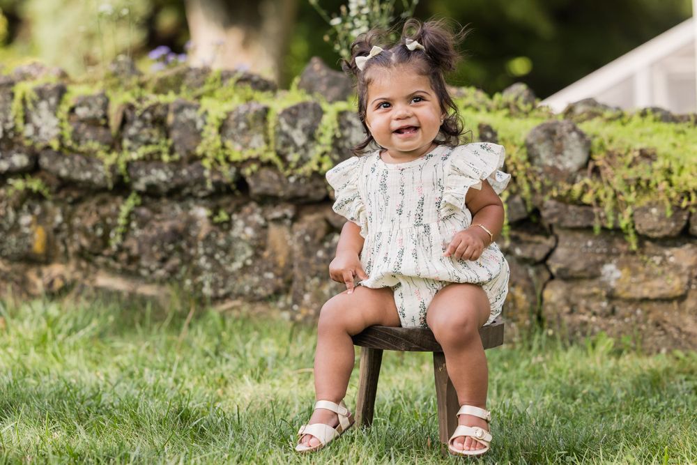 A child sits on mossy stone steps in a garden wearing a floral dress and sandals.