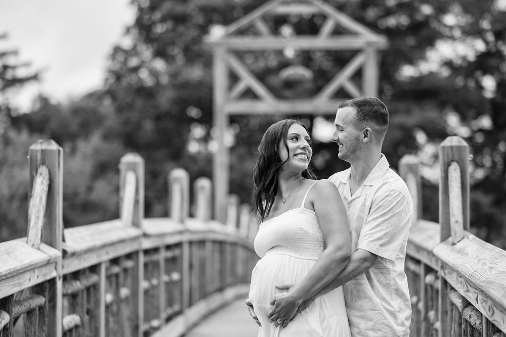 Couple embracing in romantic engagement photo shoot session on wooden bridge in black and white.