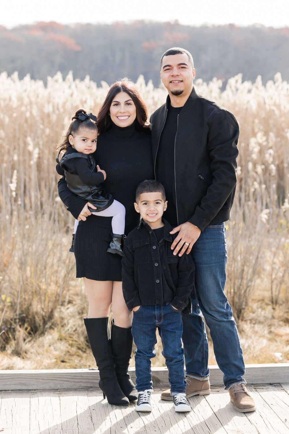 Family portrait outdoors in matching black outfits against winter field backdrop.
