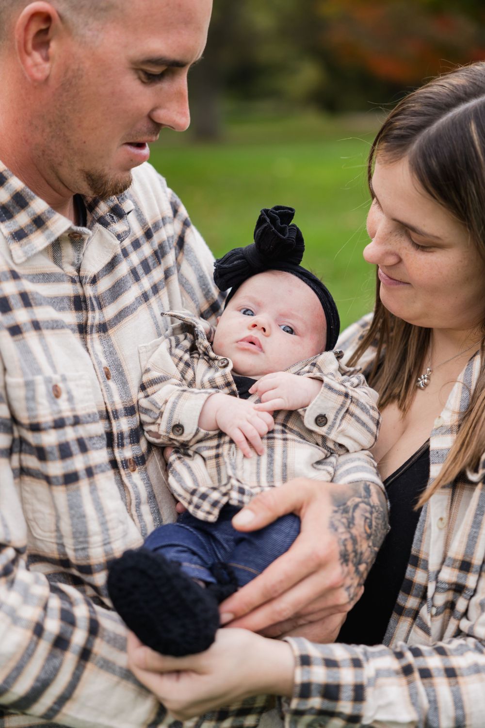 Intimate family moment with baby in plaid outfit being held by parents outdoors.