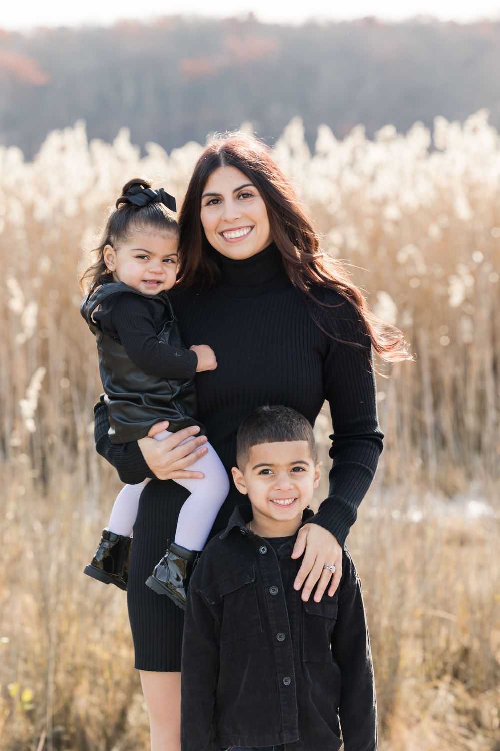 Family portrait with mother and children wearing coordinated black outfits in field of tall grass.