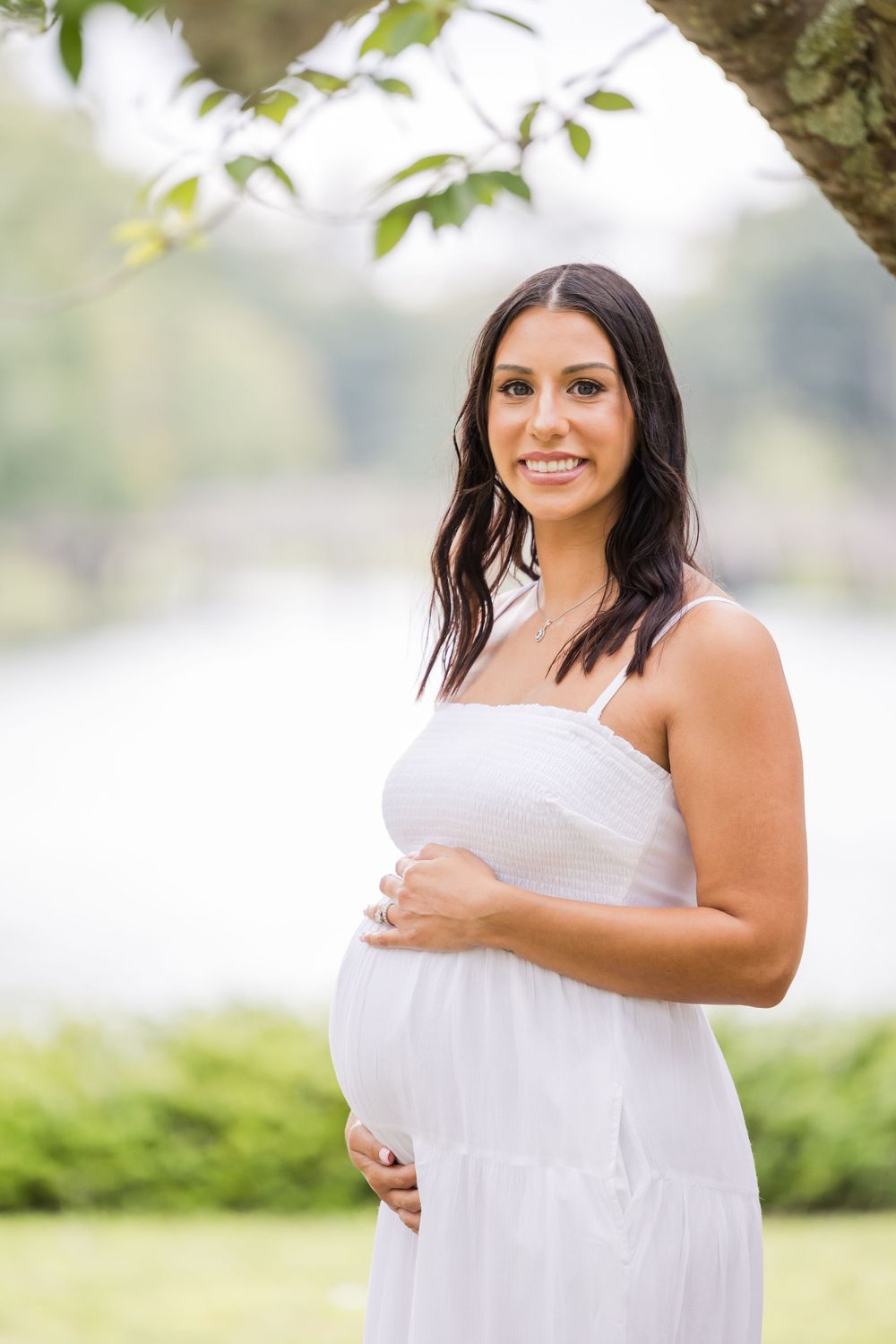 Beautiful maternity photography session in a natural outdoor setting with soft lighting and white dress.