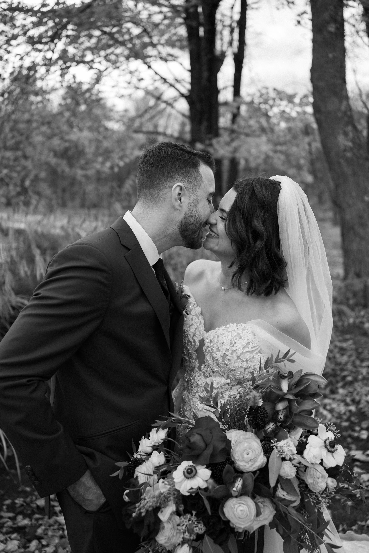 A romantic black and white wedding photo captures a couple kissing while holding a floral bouquet.