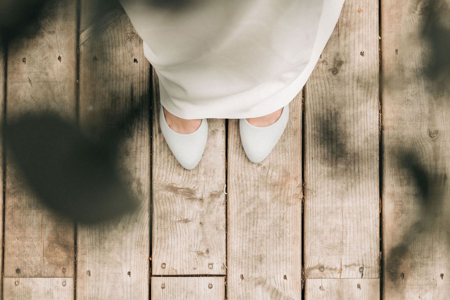 White shoes on rustic wooden floorboards with dramatic shadows cast across the planks.