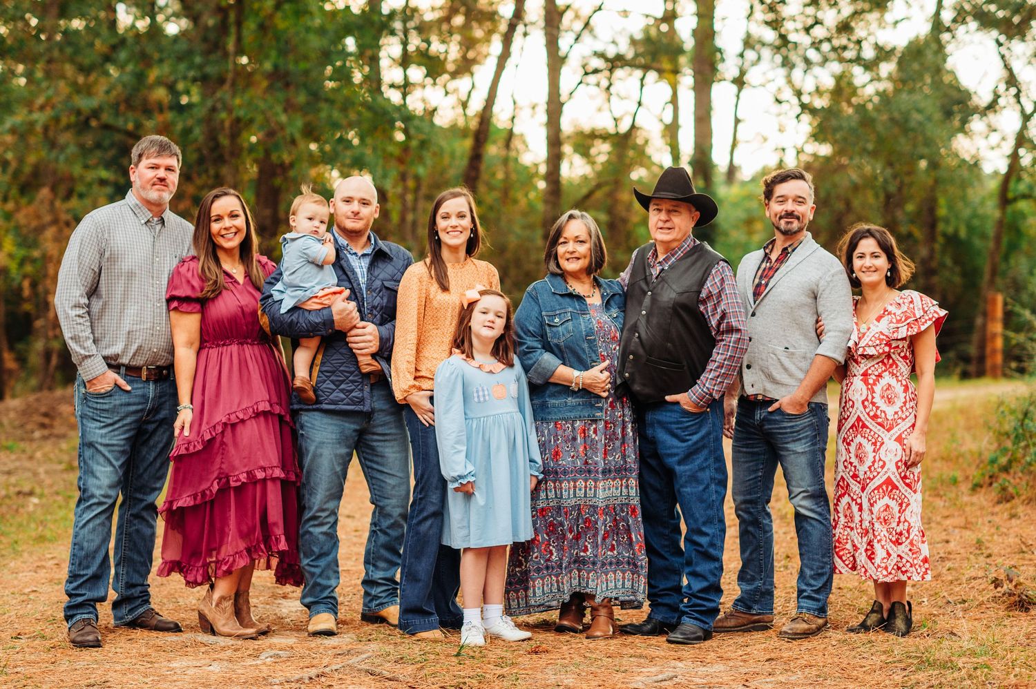 Large family in coordinated outfits poses together in outdoor wooded setting at sunset.