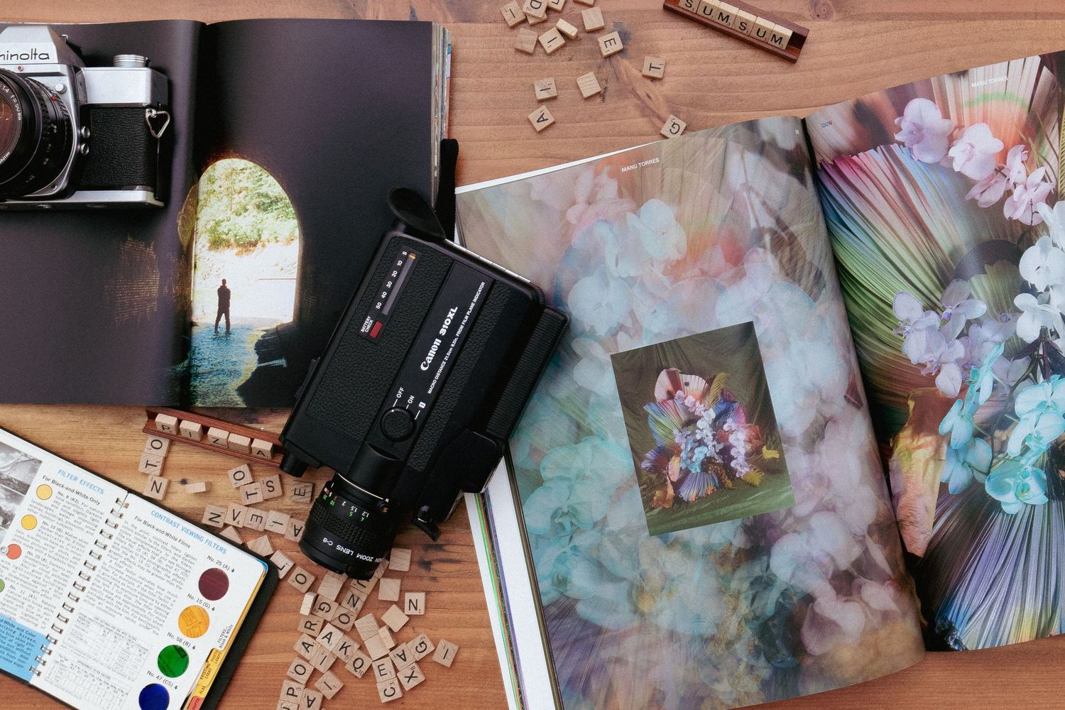 Flatlay of vintage camera, watercolors, and floral prints on wooden surface.