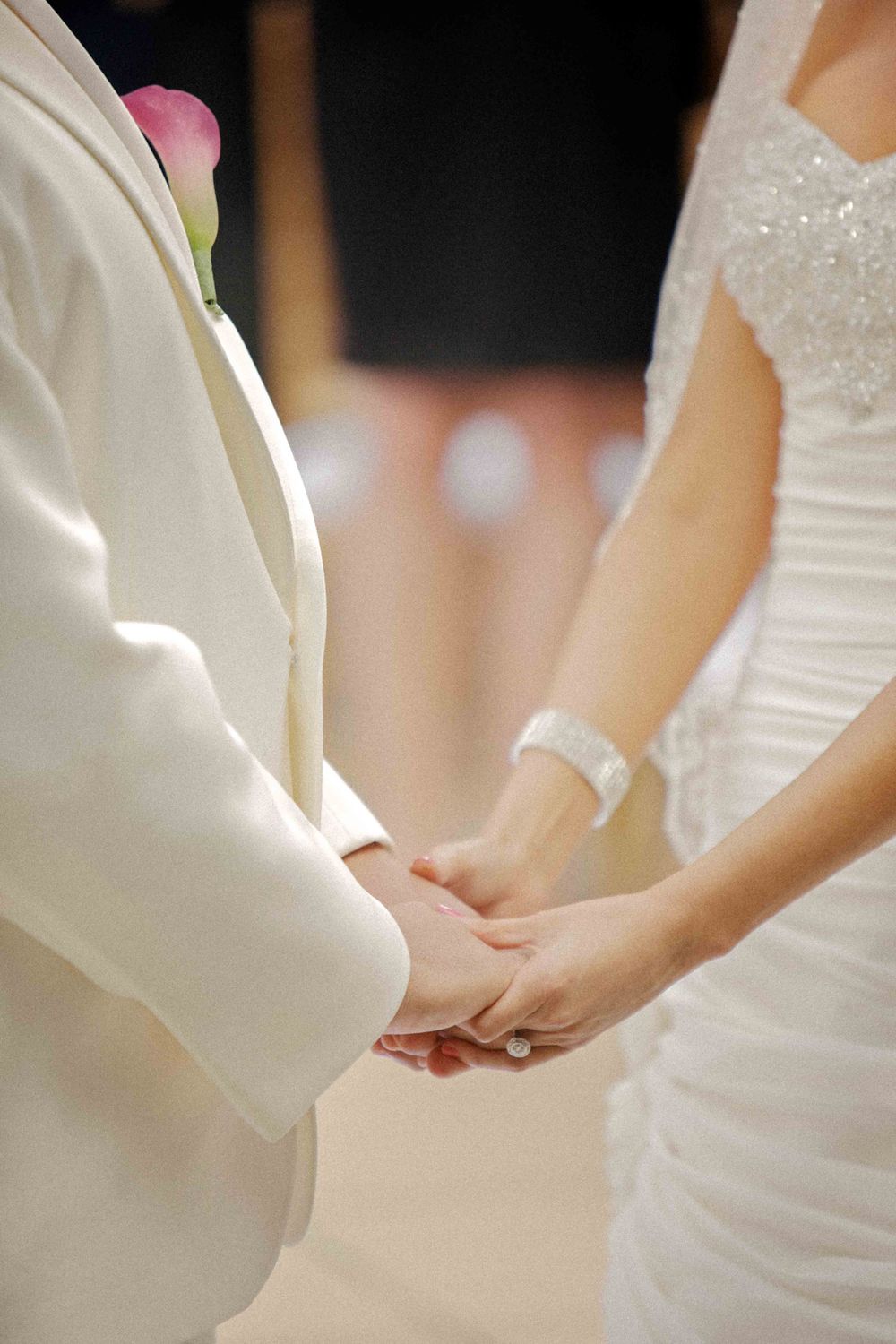 A close-up view of two people holding hands during a wedding ceremony wearing white formal attire.