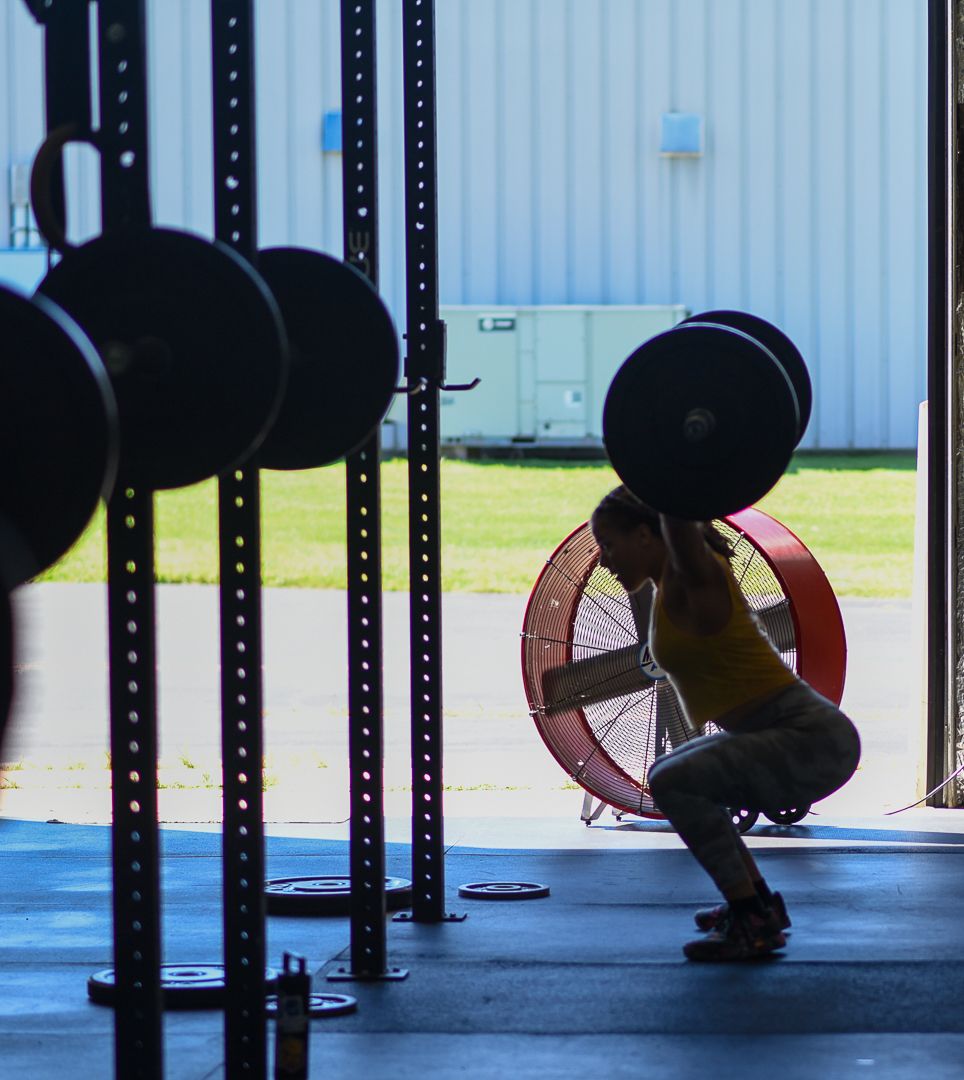 Side view of someone performing a weighted squat with a barbell in a CrossFit-style gym setting.