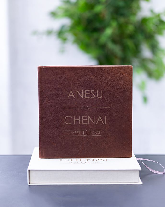 A brown leather photo album with embossed text sits on a white book against a blurred background.