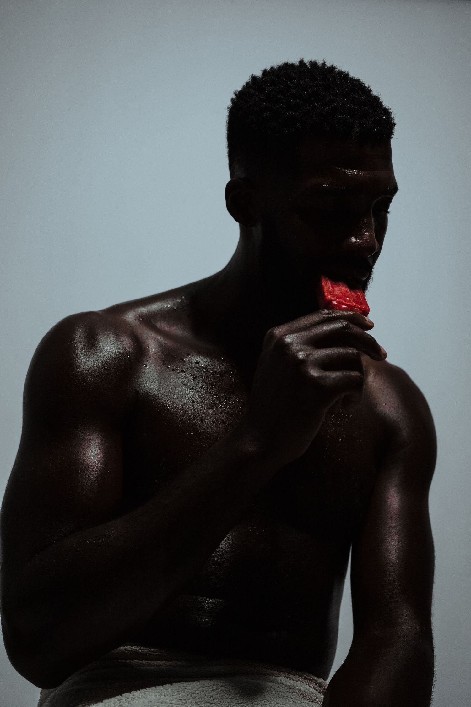 Artistic low-key portrait of a silhouetted figure holding a red object against grey background.