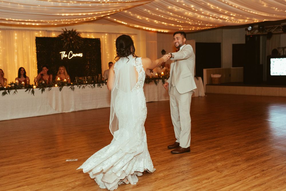 First dance moment on wooden dance floor at an elegantly lit wedding reception.