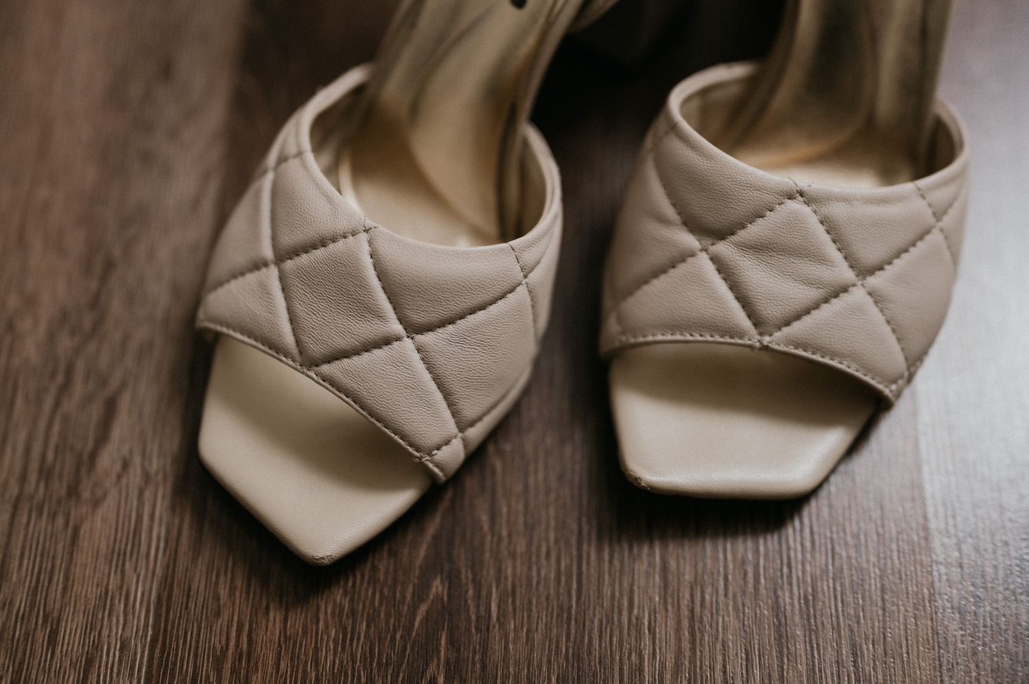 Elegant quilted cream sandals with delicate straps displayed on dark wood surface.