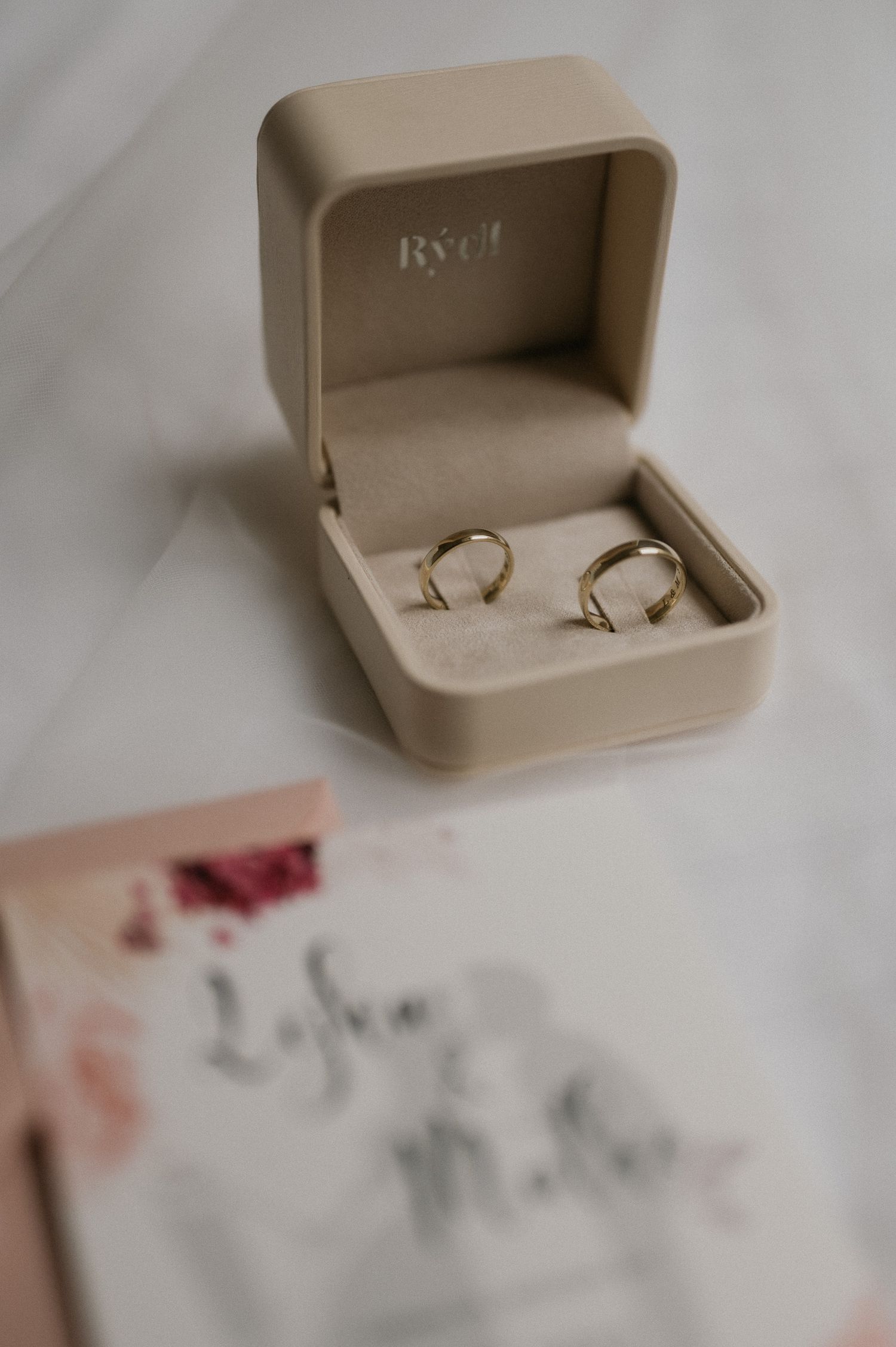 Wedding rings nestled in a beige ring box with soft fabric background.