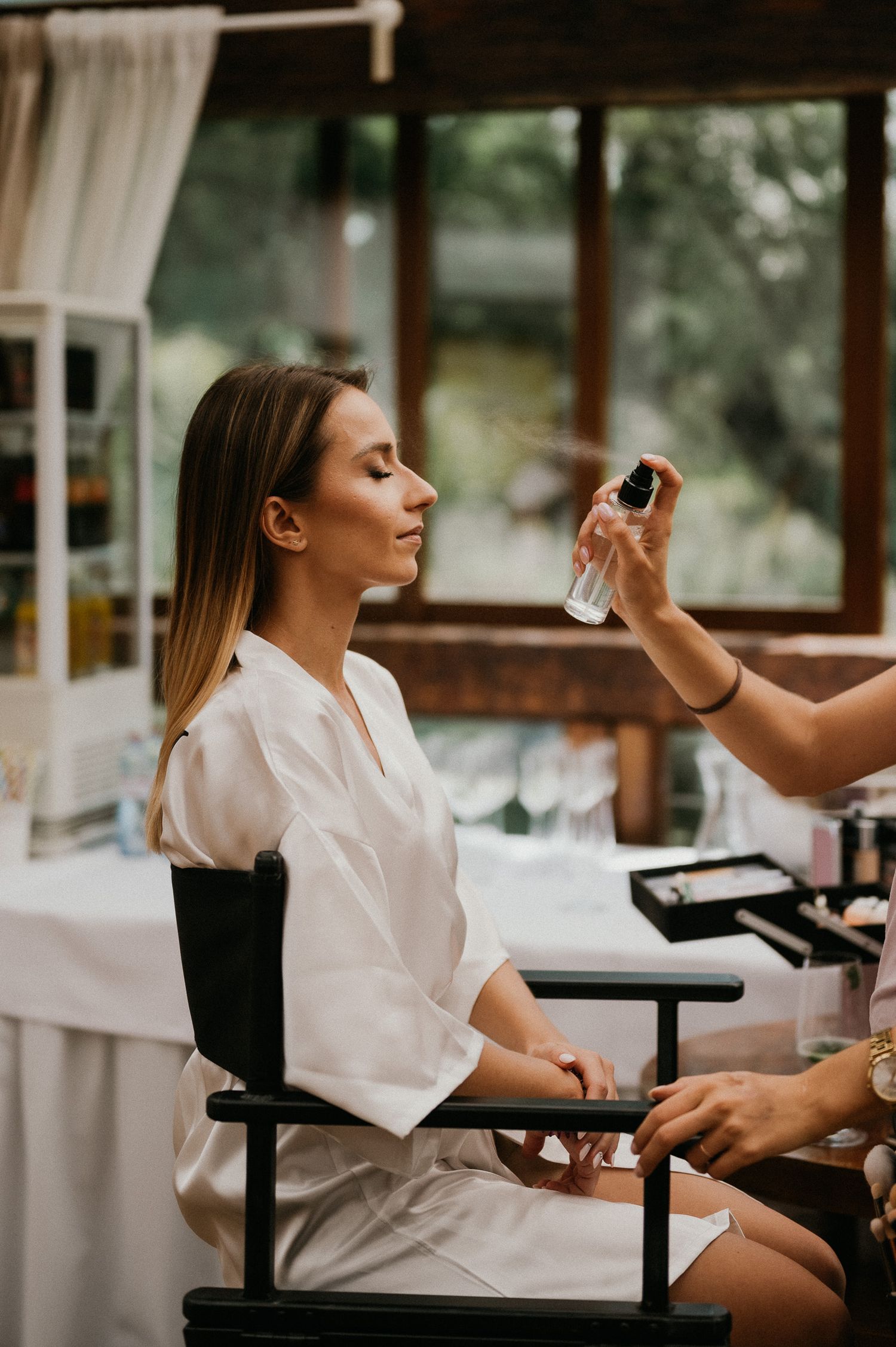 Getting ready scene with makeup application in a sunlit room with white decor.