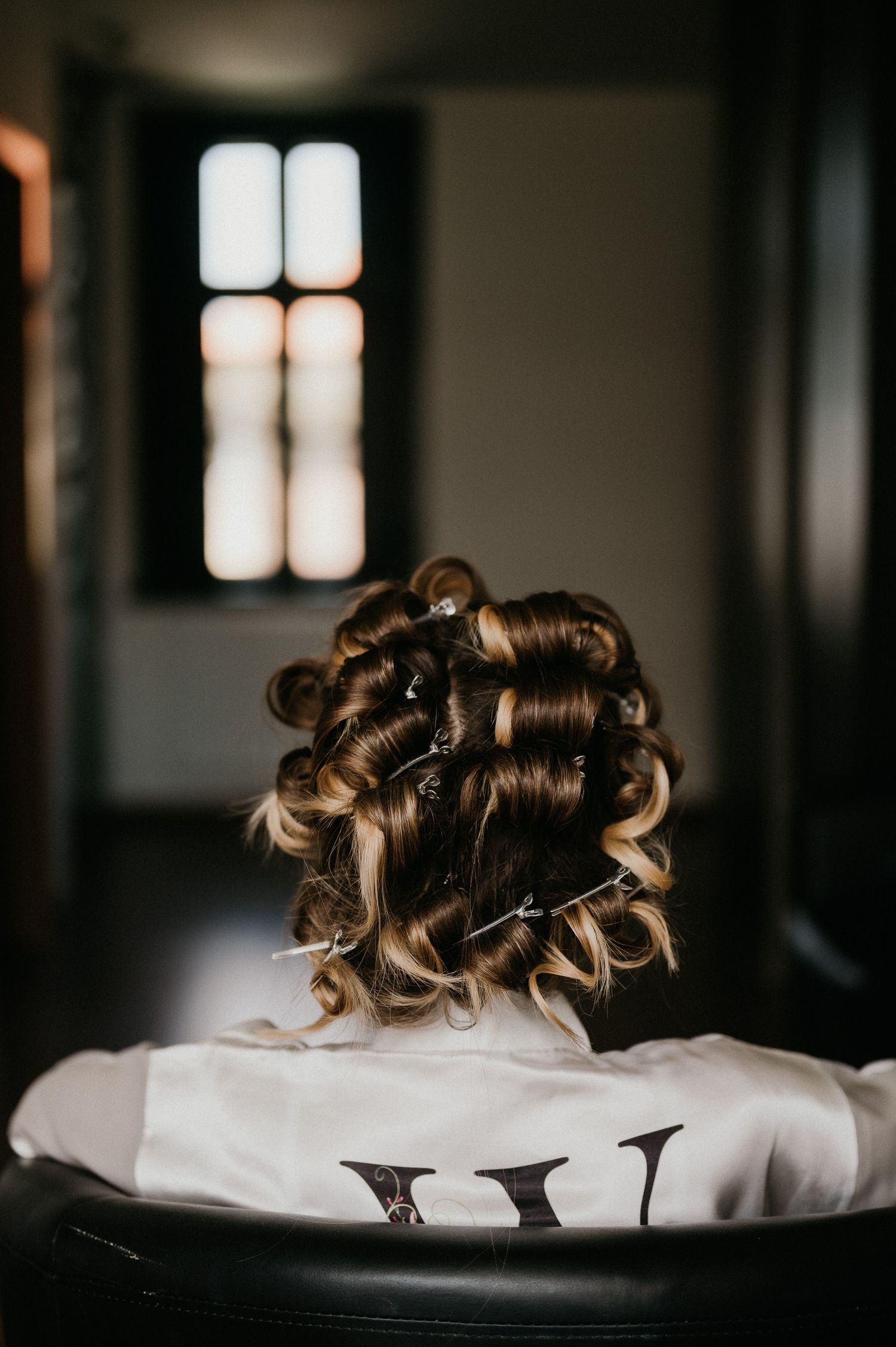 Styled curls in progress sitting on a salon chair with window light in background.