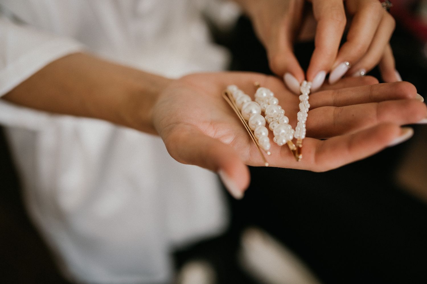 Close-up of hands holding delicate pearl hair accessories against white fabric.